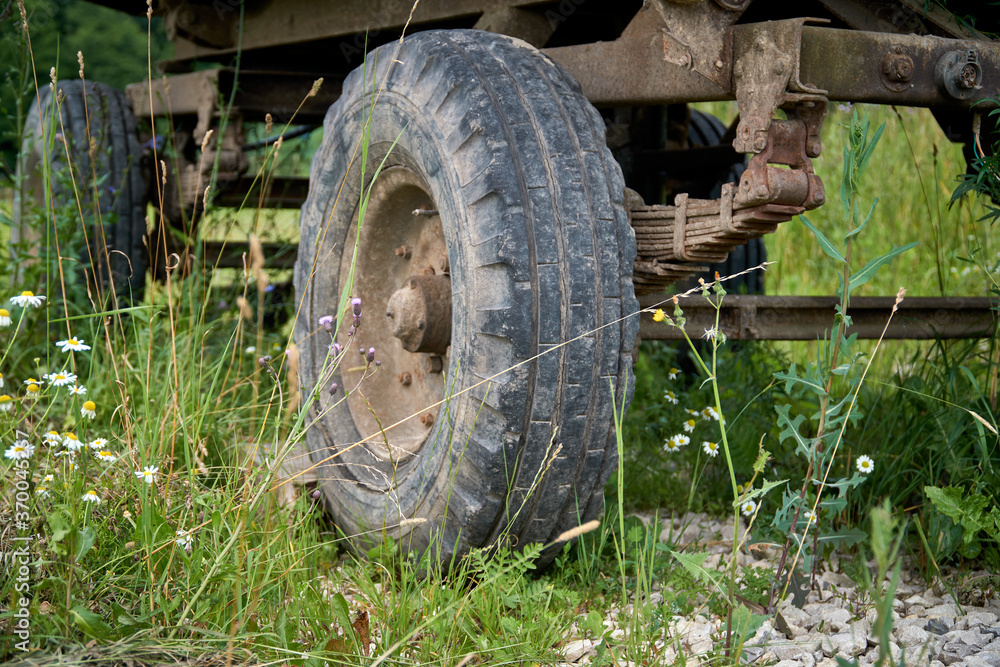 An abandoned old cargo trailer stands in a field on green grass. Trailer wheel and chassis close up An abandoned old cargo trailer stands in a field on green grass. Trailer wheel and chassis close up
