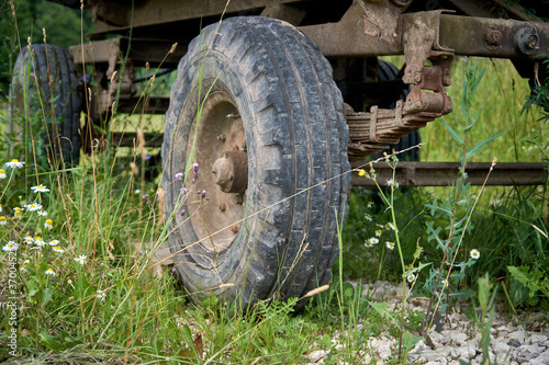 An abandoned old cargo trailer stands in a field on green grass. Trailer wheel and chassis close up
