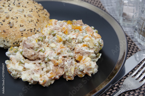 Tuna salad in black plate. Ingredients: tuna, carrots, eggs, onion, canned peas, croutons, mayonnaise