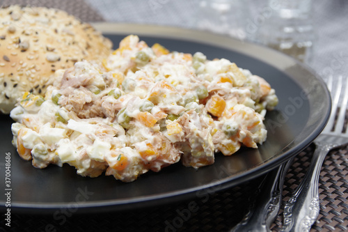 Tuna salad in black plate. Ingredients: tuna, carrots, eggs, onion, canned peas, croutons, mayonnaise