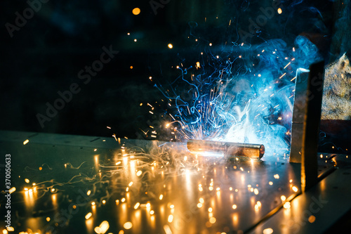 A man with a welding machine in gloves welds an iron door. Lots of caviar and smoke