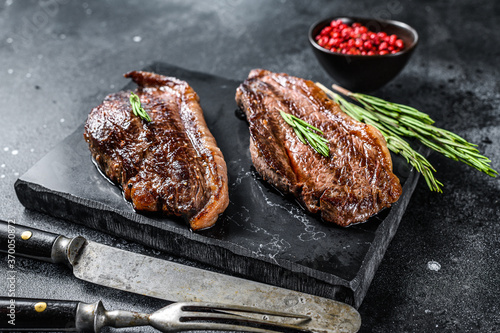 Grilled top sirloin cap or picanha steak on a stone chopping Board. Black background. Top view photo