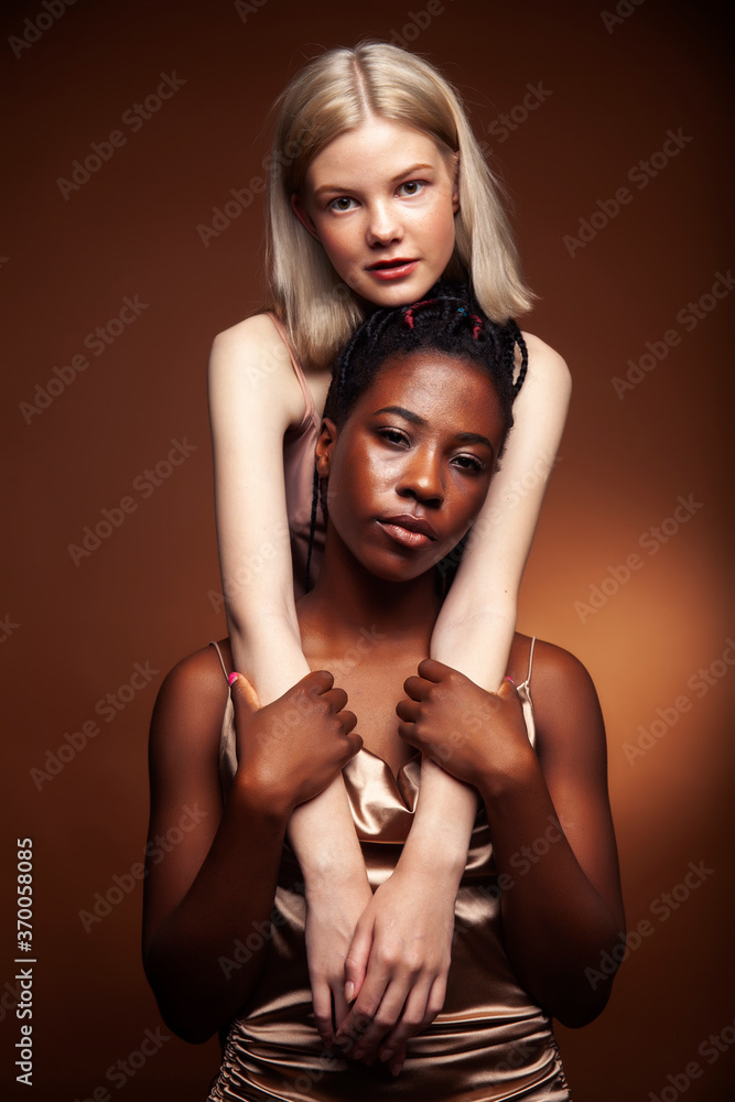 two pretty girls african and caucasian blond posing cheerful together on browm background, etnithity diverse lifestyle people concept two pretty girls african and caucasian blond posing cheerful together on browm background, etnithity diverse lifestyle people concept