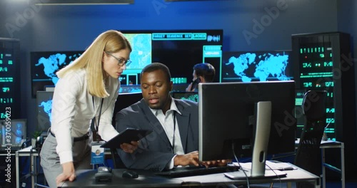 Wallpaper Mural Caucasian woman asking for advice, demonstrating data on tablet device to African American man sitting at computer. Female and male multiethnic colleagues discussing work in cyber center. Multiethnic. Torontodigital.ca