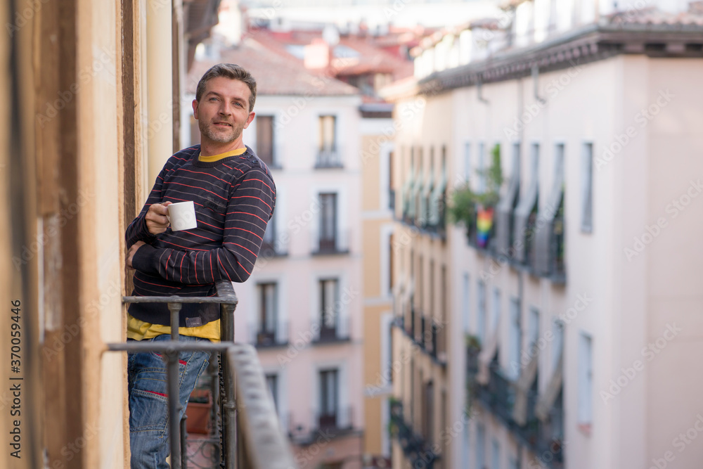 30s or 40s attractive and happy man at home balcony relaxed and cheerful enjoying cup of coffee looking to city street smiling and enjoying the urban view