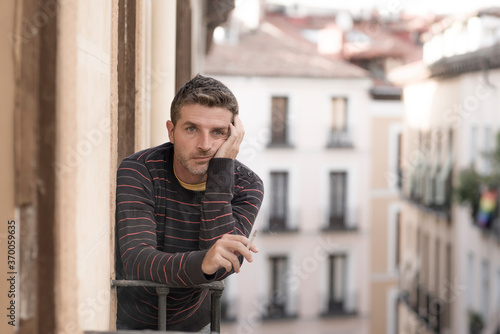 urban lifestyle emotional portrait of young handsome man sad and depressed smoking cigarette thoughtful at home balcony leaning unhappy feeling bittered suffering some problem