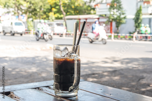 Vietnamese cold coffee with ice in a habitual glass mug. On the wooden table at a street cafe, for 10 000 dongs (0.4$) in District 4, Ho Chi Minh City, Vietnam. With a street in the background.
