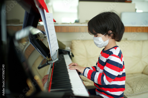 Child wearing face mask playing piano at home.Fingers on keys.Boy with facemask having music lesson.Young male musical homeschooling.String instrument. Facemask.