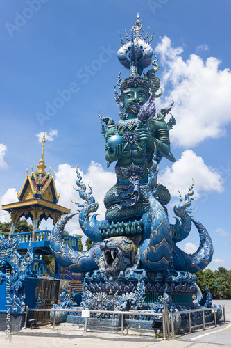 Chiangrai, Thailand - June 7, 2020: Blue God Statue Hold Lotus and Ball on Blue Sky Background with Natural Light in Wat Rong Suea Ten Temple © steafpong