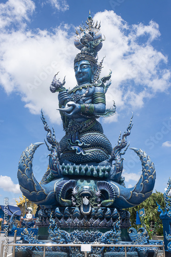 Chiangrai, Thailand - June 7, 2020: Blue God Statue Hold Lotus on Blue Sky Background with Natural Light in Wat Rong Suea Ten Temple at Side View