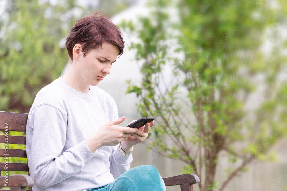 A girl in home clothes sitting on a bench with a smartphone in her hand A girl in home clothes sitting on a bench with a smartphone in her hand