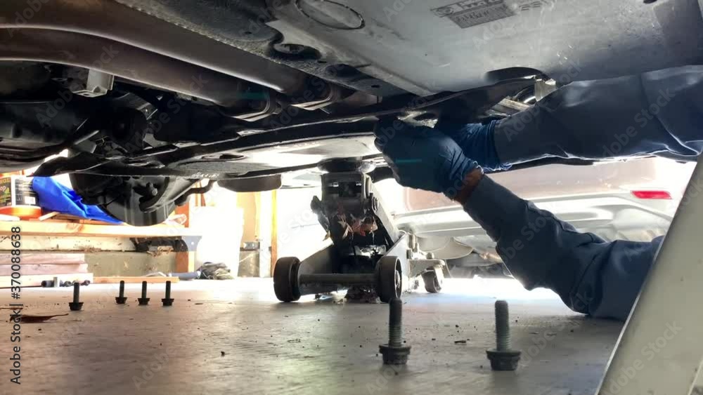 Mechanic Working Under Car Loosening Bolts Mechanic Working Under Car Loosening Bolts