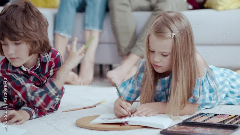 Cute beautiful focused kids brother and sister drawing pictures and painting colored pencils on the floor. Childhood. Activities. Hobby. Teamwork concept.