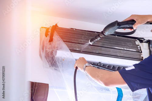 The technicians are cleaning the air conditioner by spraying water. Hand and water spray are cleaning the air conditioner.