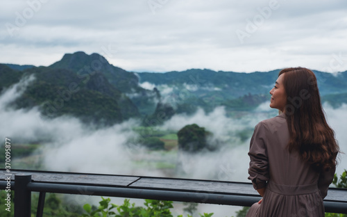 Rear view image of a female traveler looking at a beautiful foggy mountain and nature view