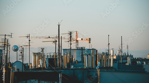 Rooftops with dozens of metal chimneys and antennas at sunrise. Construction crane in the background. Krakow, Poland.