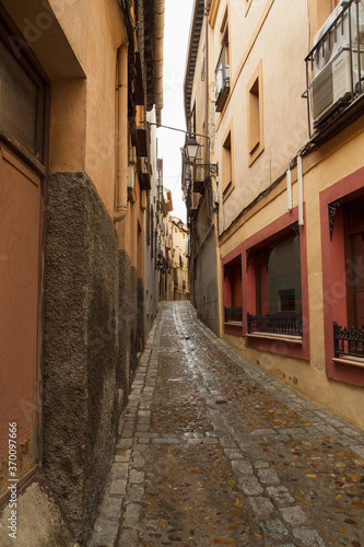 Fototapeta Naklejka Na Ścianę i Meble -  Cityscape. History and architecture. Colorful buildings with ancient design. View of the narrow alley and wet street after rain, in Toledo, Spain.