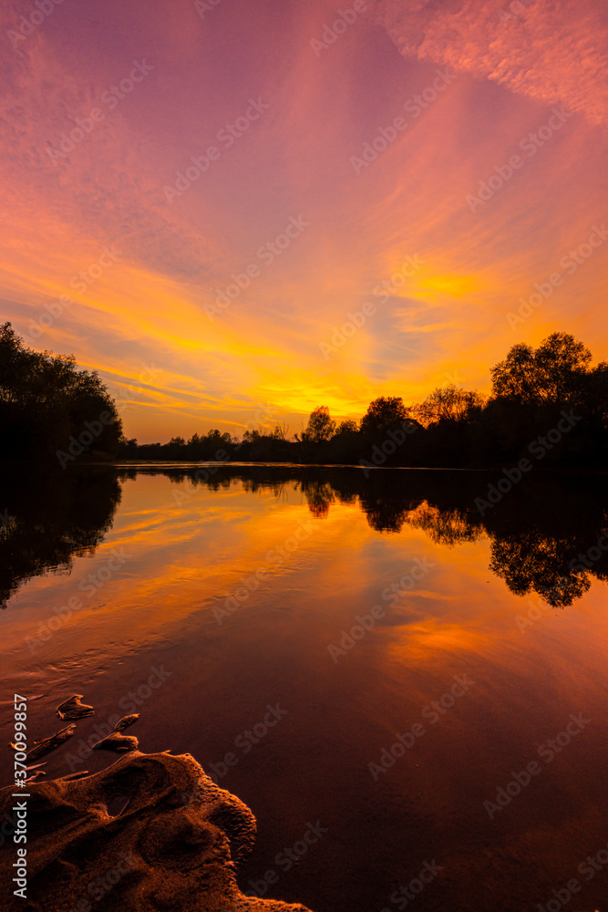 Wild, colorful sunset over tranquill river in a remote area in Europe