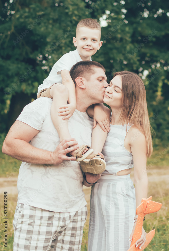 Family resting in nature, dad keeps the boy around his neck and kisses mom Family resting in nature, dad keeps the boy around his neck and kisses mom