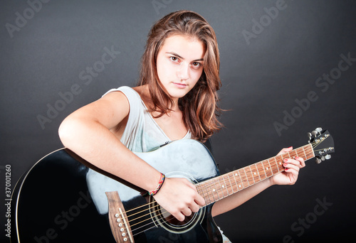 Portrait of young young beautiful girl with long hair playing an black acoustic guitar on black background 