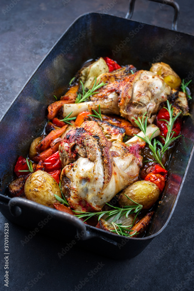 Traditional geschmorte Lammhaxe mit Auberginen, Kartoffel und Tomaten angeboten als close-up in einer rustikalen Schmorpfanne