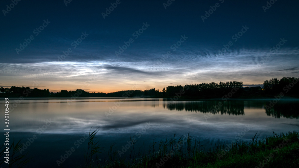 night landscape with white silver clouds over the lake, blurred foreground, charming cloud reflections in the lake water, summer night