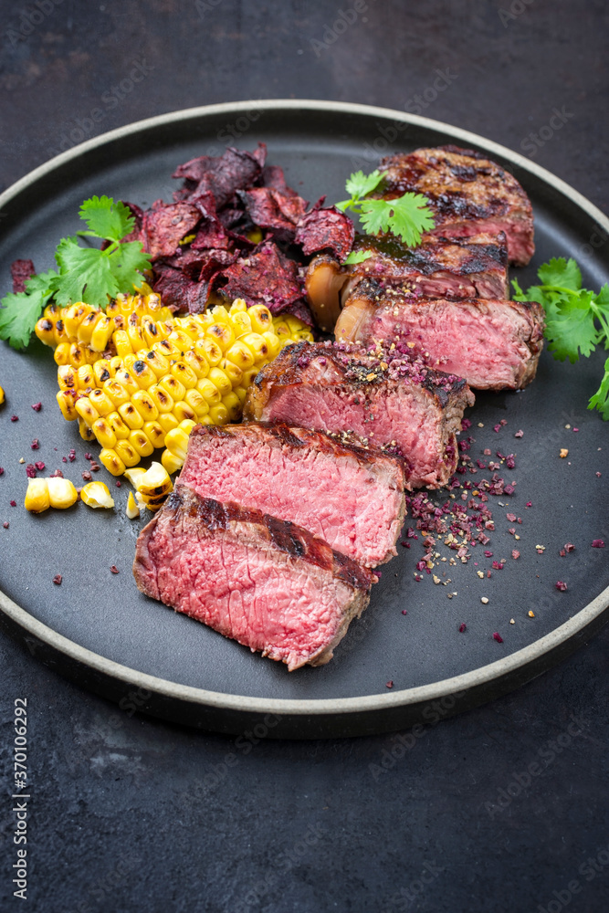 Barbecue dry aged wagyu roast beef steak with corn and vegetable chips offered as close-up on a modern design plate Barbecue dry aged wagyu roast beef steak with corn and vegetable chips offered as close-up on a modern design plate