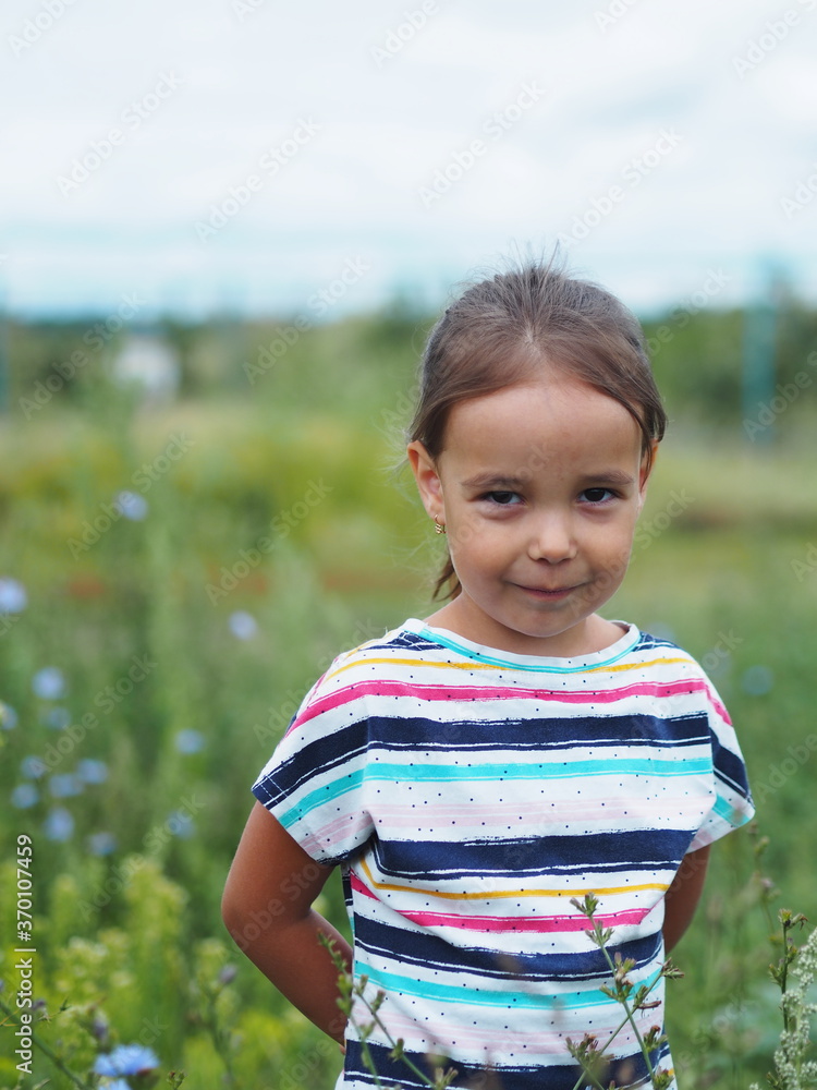 A little girl walks and looks at the plants in the field and smiles.Child's communication with nature. A little girl walks and looks at the plants in the field and smiles.Child's communication with nature.