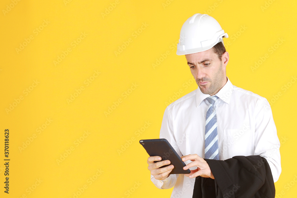 Handsome and smart engineer in suit and white shirt and Wearing a white safety engineer hat with hand holding smartphone isolated on yellow background. Copy Space