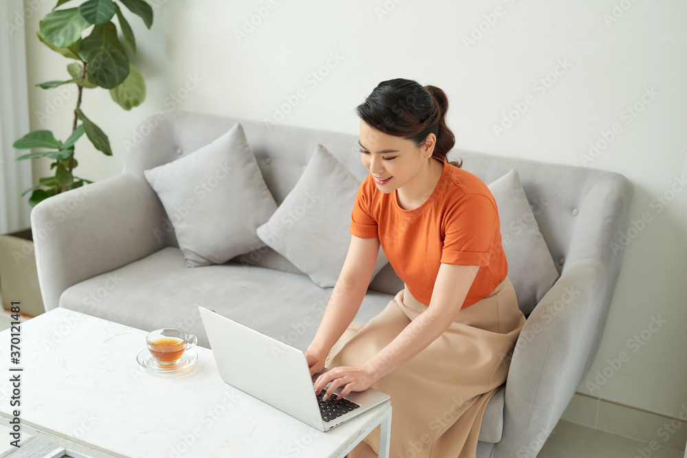 Young woman relaxing at home on the couch, she is having a tea and using a laptop Young woman relaxing at home on the couch, she is having a tea and using a laptop