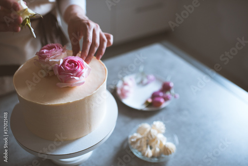Fotografie Woman making cake decorating with flower roses staying on kitchen table close up at home