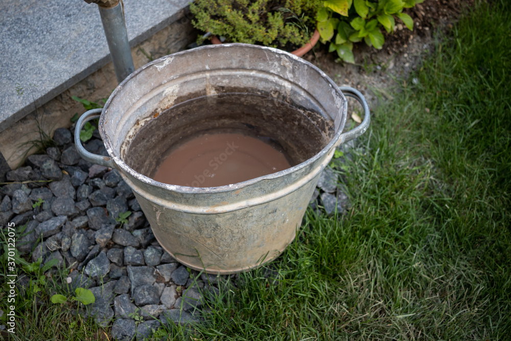 Metal bucket filled with water and dirt on the bottom of it in a park AM