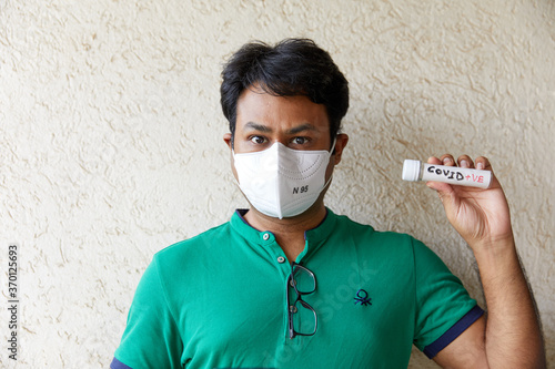 Colored man wearing a holds a Covid Negative (Covid -ve) blood sample bottle