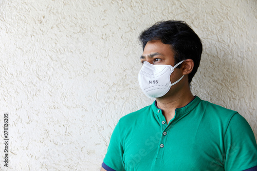 Mid Shot of Adult South Asian Indian Male wearing N95 white respirator and green polo t-shirt with Face looking left of camera