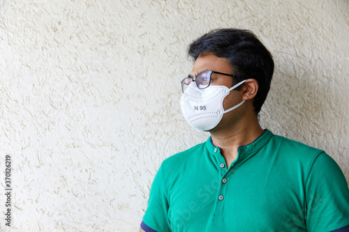 Mid Shot of Adult South Asian Indian Male wearing green t-shirt and an N95 white respirator with Body and Face looking off camera