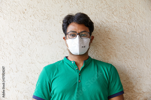 Mid Shot of Adult South Asian (Indian) Male wearing green t-shirt and an N95 white respirator with Body and Face facing and the camera- Anti Viral, Anti Pollution, Sanitized, Mask