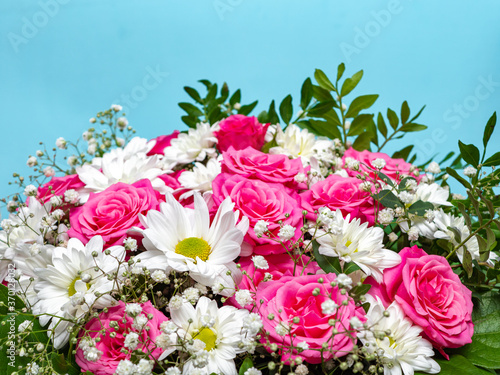 Beautiful pink roses and white daisies in a box on a blue background.