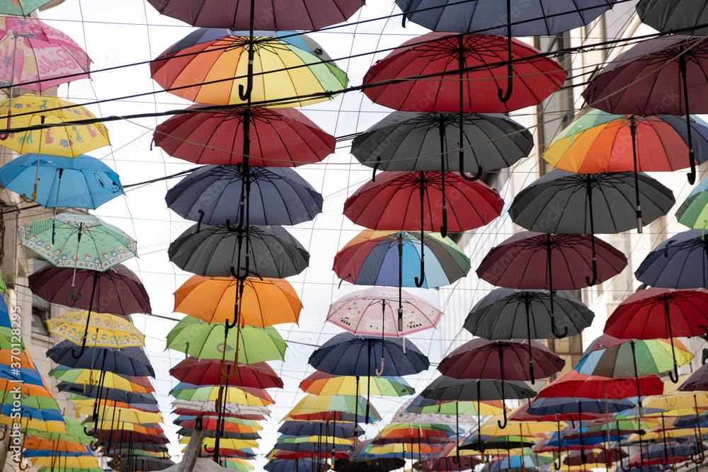 A group of different colored umbrella placed next to each other above the street in different colors and shades