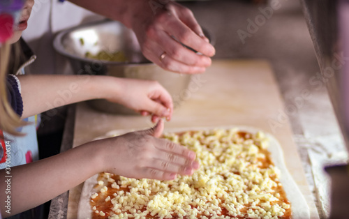 The hands of a child and an adult sprinkle cheese on pizza; we prepare at home with children, training courses