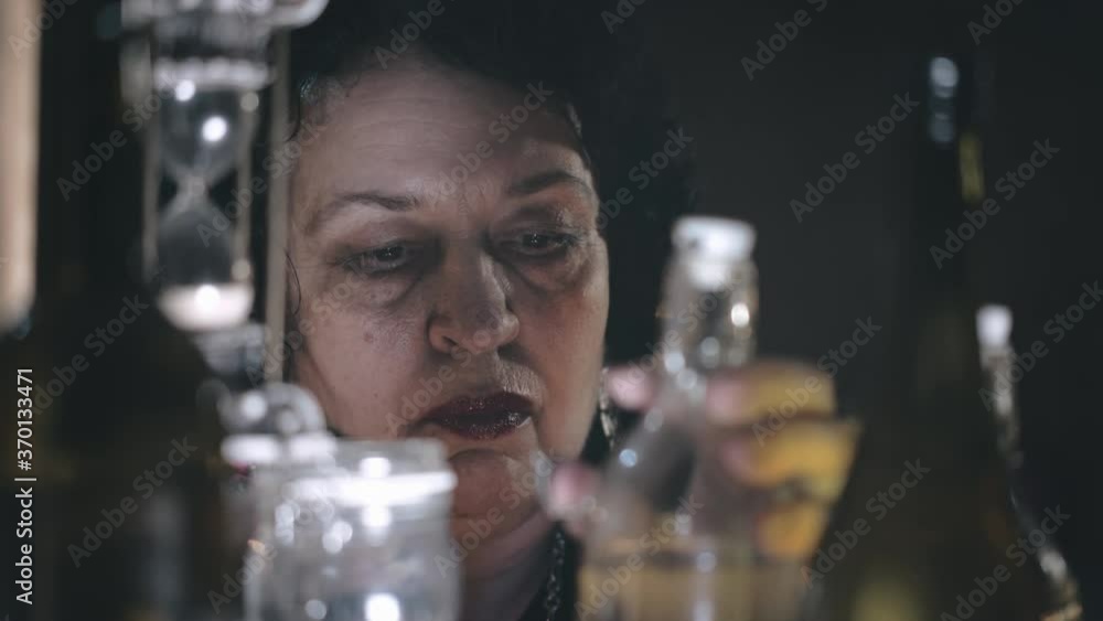 Old witch looking through glass bottles with potions Old witch looking through glass bottles with potions