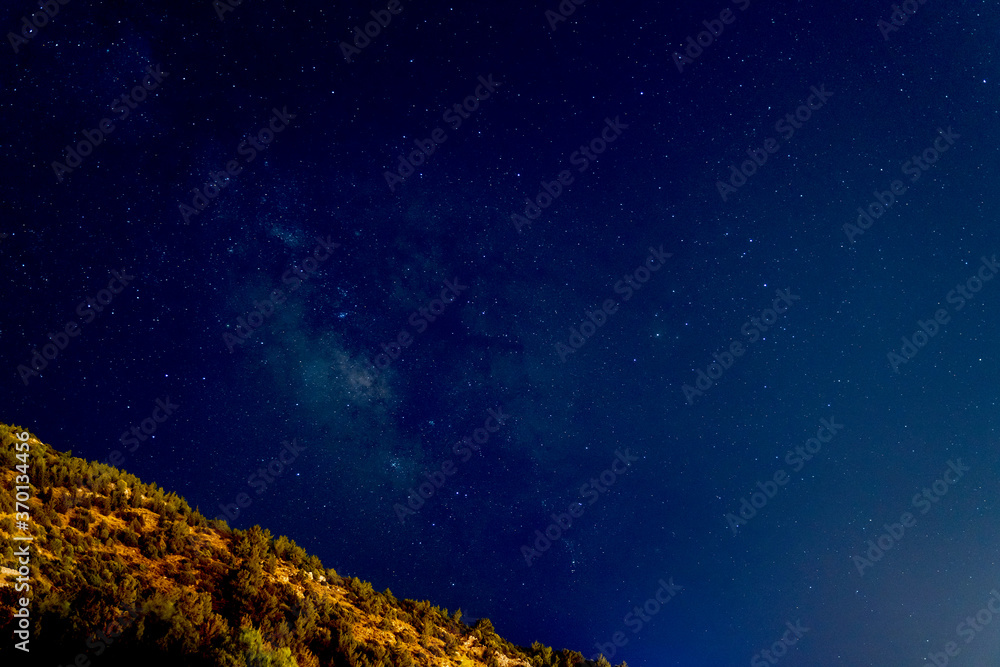 Night sky with many shiny stars, milky way. View of a wooded hill