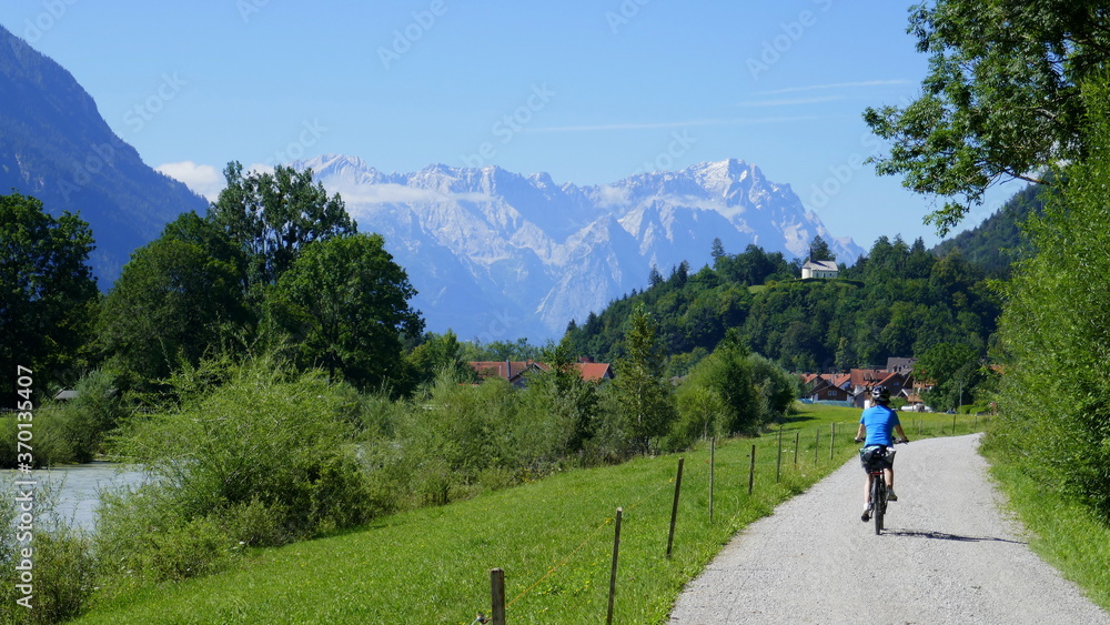 Radlerin auf dem Loisach Fernradweg in Richtung Garmisch-Partenkirchen mit Loisach und Zugspitzmassiv, Bayern
