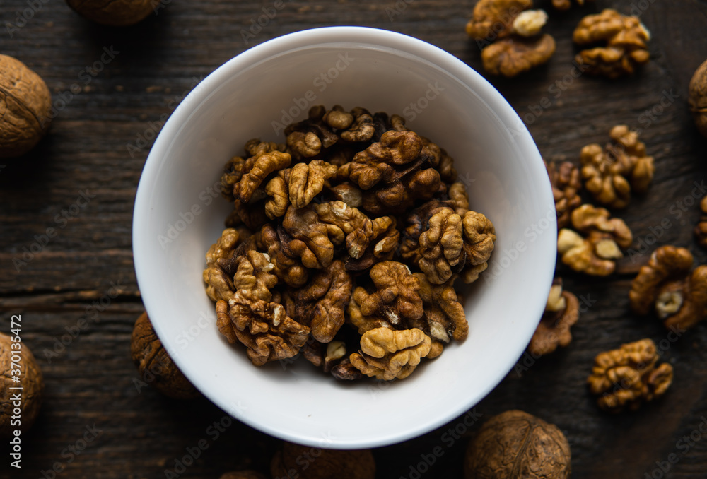 Walnut in a smale plate with scattered shelled nuts and whole nut which standing on a wooden vintage table. Walnuts is a healthy vegetarian protein nutritious food. Walnut on rustic old wood. Walnut in a smale plate with scattered shelled nuts and whole nut which standing on a wooden vintage table. Walnuts is a healthy vegetarian protein nutritious food. Walnut on rustic old wood.