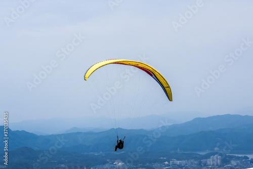 Paraglider flying against the blue sky with colorful wing above the clouds.