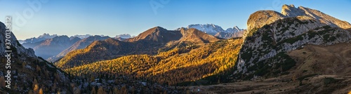 Sunny colorful autumn alpine Dolomites rocky mountain scene, Sudtirol, Italy. Peaceful view from Falzarego Pass. Snowy Marmolada massif and Glacier in far. High resolution ultra wide panorama.
