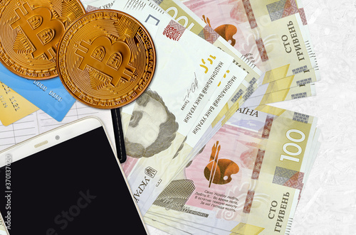 100 Ukrainian hryvnias bills and golden bitcoins with smartphone and credit cards. Cryptocurrency investment concept. Crypto mining or trading photo