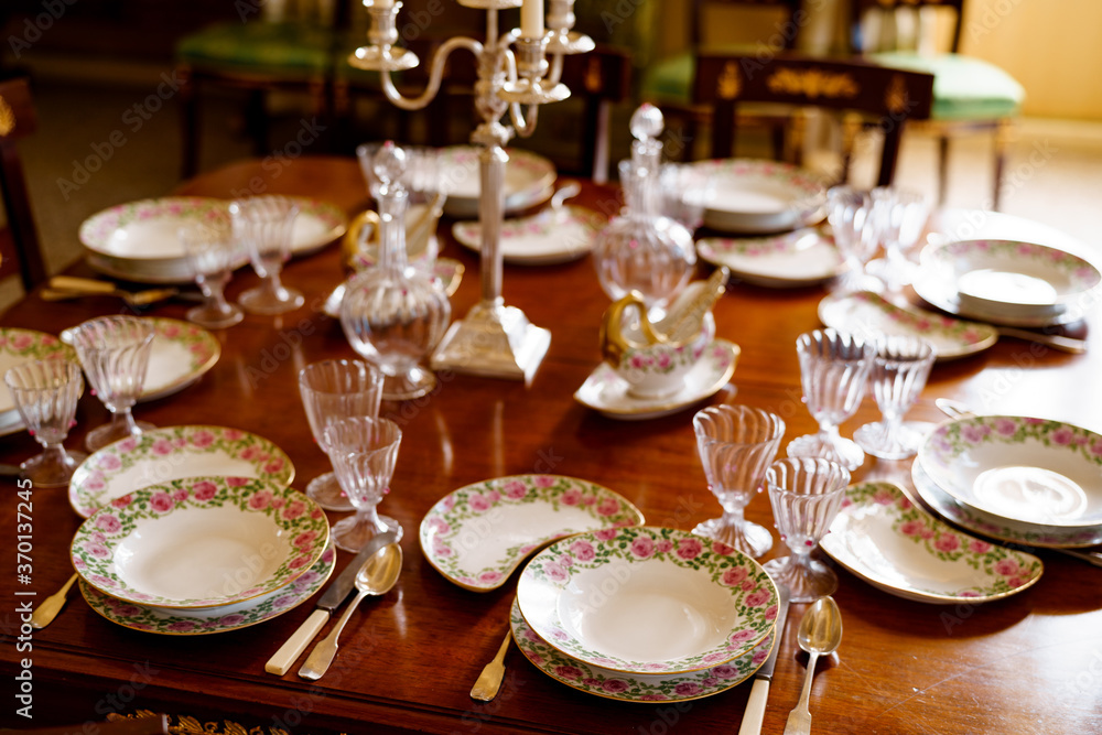 Festive table setting with plates, spoons, knives, glasses, decanters and a candlestick in the center on a wooden table.