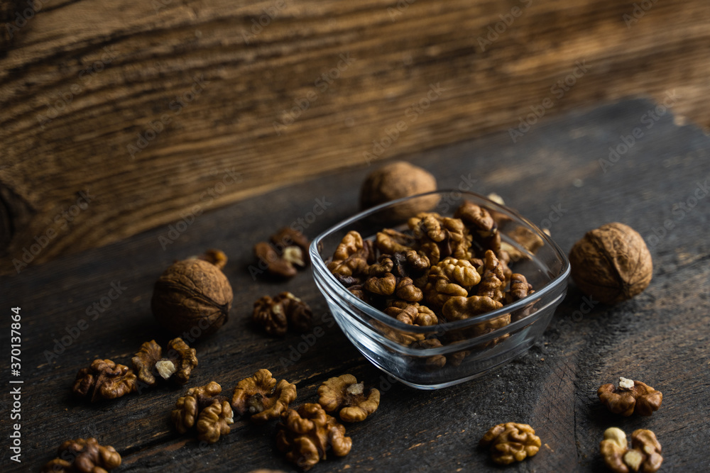 Walnut in a smale plate with scattered shelled nuts and whole nut which standing on a wooden vintage table. Walnuts is a healthy vegetarian protein nutritious food. Walnut on rustic old wood. Walnut in a smale plate with scattered shelled nuts and whole nut which standing on a wooden vintage table. Walnuts is a healthy vegetarian protein nutritious food. Walnut on rustic old wood.
