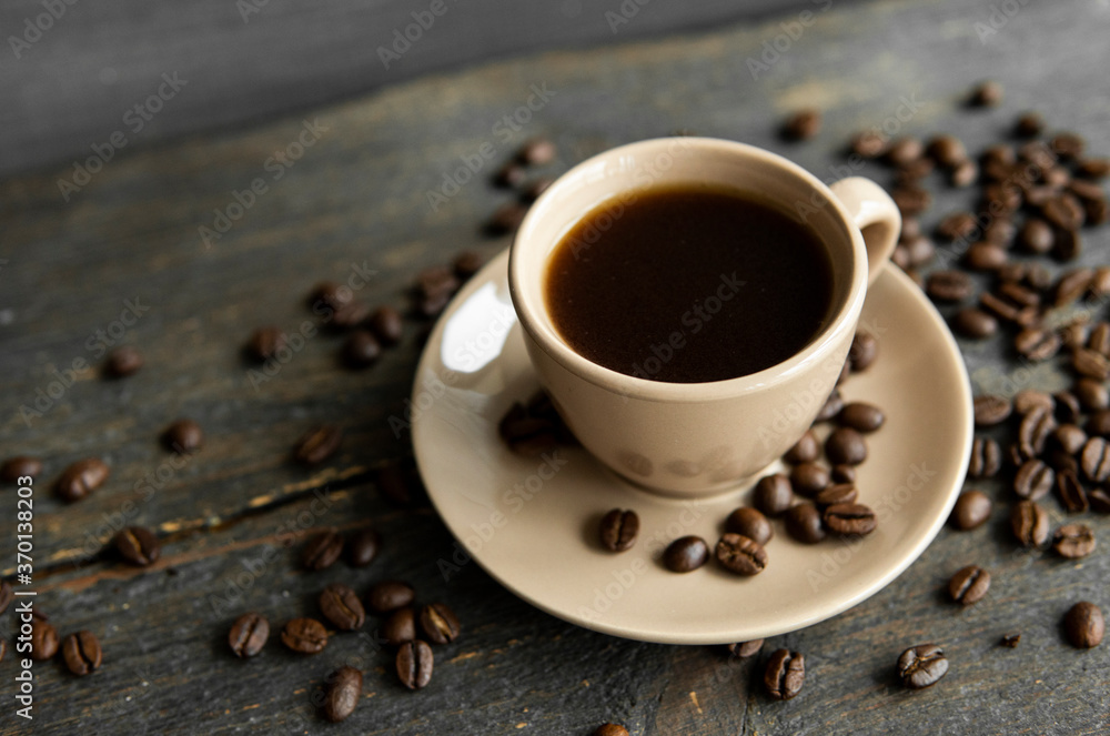 Coffee cup with roasted coffee beans on wooden table background. Mug of black coffe with scattered coffee beans on a wooden table. Fresh coffee beans.