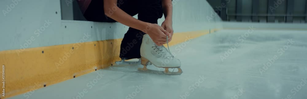 Professional teenager boy figure skater tying laces on skates before training on indoor ice arena. Shot on RED cinema camera with 2x Anamorphic lens, 75 FPS Slow motion Professional teenager boy figure skater tying laces on skates before training on indoor ice arena. Shot on RED cinema camera with 2x Anamorphic lens, 75 FPS Slow motion